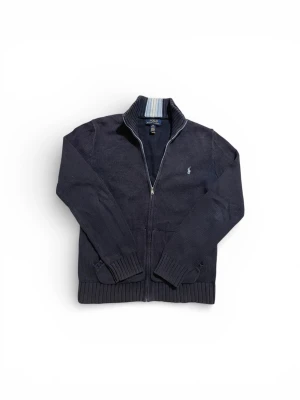 Polo Ralph lauren hel zip  - Snygg mörkblå stickad kofta från Polo Ralph Lauren med dragkedja framtill och ribbade muddar. Klassisk logga broderad på bröstet och krage med ljusblå och vita ränder på insidan. Perfekt för lager-på-lager-stil. Tveka inte att höra av er vid frågor