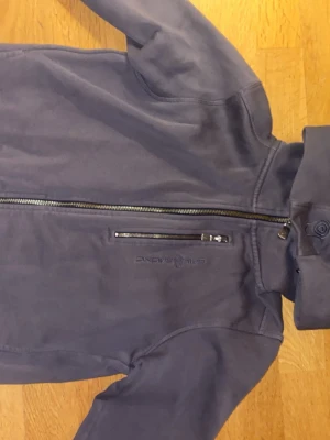 Grå Sail Racing jacka med dragkedja - Snygg grå hoodie från Sail Racing med broderad logga på bröstet och ärmen.tröja har hel dragkedja framtill och en extra ficka med dragkedja på bröstet. Tillverkad i mjuk bomull och har en stilren, sportig look.