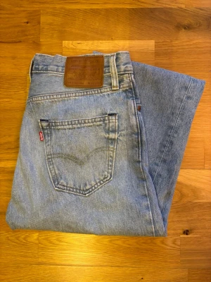 Levi's Stay Loose ljusblå jeans W29 L32 - Ljusblå jeans från Levi's i modellen Stay Loose med klassisk femficksdesign och brunt läderpatch bak. Jeansen har en loose passform och raka ben, tillverkade i slitstarkt bomullsdenim. Perfekt för dig som gillar avslappnad stil och vintagevibe. OBS, KNAPPT AMVÄNDA. 