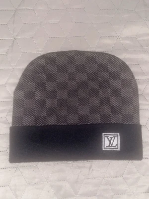 Rutig mössa i grått och svart - Säljer en snygg mössa i mörkgrått och svart med rutig design. Mössan har en bred svart kant, och är tillverkad i ett mjukt, stickat material. Perfekt för dig som vill ha en lyxig accessoar med street vibe.