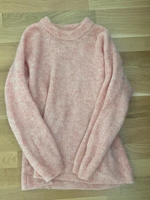 Rosa stickad tröja från Lindex - Mysig stickad tröja från Lindex i ljusrosa ton. Tröjan har en rund halsringning och långa ärmar.