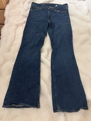 Bootcut jeans i mörkblå denim - Bootcut jeans från &Denim i mörkblå tvätt med hög midja. Klassisk femficksmodell med dragkedja och knapp framtill. Jeansen har en snygg bootcut-passform och är tillverkade i slitstark denim. Perfekt för dig som gillar retrovibbar och vill ha ett coolt snitt.