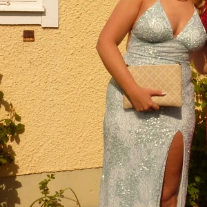 Ljusblå glittrig långklänning - Säljer en min superfina ljusblå långklänning med glittriga paljetter. Klänningen har en öppen rygg, smala axelband och en hög slits framtill. Materialet är glittrigt och festligt, perfekt för bal! 