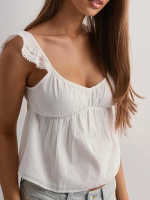 Vit blus med spetsdetaljer från Nelly - Supersöt vit blus från Nelly med volangprydda axelband och spetsdetaljer. Toppen har en öppen rygg med stor rosett och är tillverkad i mjuk bomull. Perfekt för sommarens alla tillfällen, matcha med jeans eller kjol för en fräsch look. Den är aldrig använd o ligger i orginalförpackningen. Hör av er om ni vill ha fler bilder