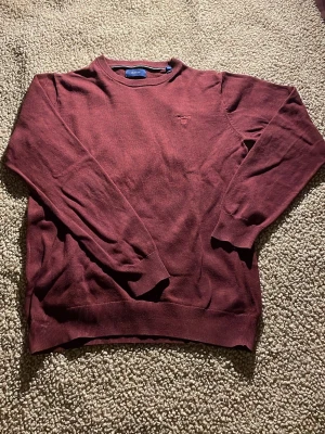 Vinröd stickad tröja från GANT - Snygg vinröd stickad tröja från GANT i storlek S. Tröjan har rund hals, ribbade muddar och ett diskret broderat GANT-logo på bröstet. Perfekt för dig som gillar klassisk stil med en modern touch. Inga defekter överhuvudtaget nästan helt ny! 