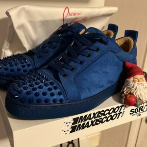 Blå sneakers från Christian Louboutin - Snygga blå sneakers från Christian Louboutin i mocka med coola nitar på tån och klassisk röd sula. Skorna har snörning och en rund tå, samt en platt sula. Perfekta för dig som vill sticka ut med en lyxig och edgy stil.