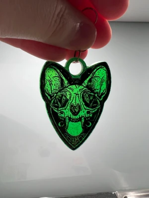 Glittriga gröna svarta djurkranium örhängen  - Unika örhängen i färgen grönt med glitter och ett coolt djurkranium motiv i svart. Formen är hjärtliknande med spetsig nedre kant och örhängena har metallkrokar. Perfekt för dig som gillar statement-smycken och djurmotiv.