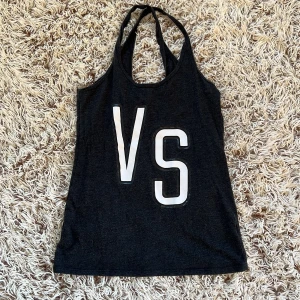Mörkgrå linnetopp från Victoria's Secret - Mörkgrå linnetopp från Victoria's Secret med stora vita bokstäver 'VS' framtill. Toppen har smala axelband och ärmlös design, perfekt för en avslappnad och sportig look. Tillverkad i mjuk bomullsblandning som känns skön mot huden. 2000-tal linne från Victoria secret. Storlek S