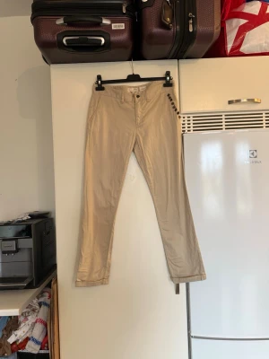 Beige chinos från Odd Molly med detaljer - Snygga beige chinos från Odd Molly med unika metallknappar längs sidan och klassisk passform. Byxorna har normal midja, raka ben och är gjorda i mjuk bomull. Perfekt för dig som gillar coola detaljer och vill sticka ut lite extra. Storlek 1 som enligt deras storleksguide motsvarar en storlek S. mer använda och kan ha små tecken på användning. 