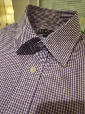 Lila rutig skjorta från Berga - Snygg lila och vit rutig skjorta från Berga i storlek M, 39/40. Skjortan har klassisk krage, vita knappar framtill och på manschetterna samt långärmad passform. Perfekt för dig som gillar stilrena detaljer och mönster.