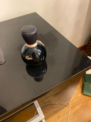 Stilren Lacoste parfymflaska - Snygg parfymflaska från Lacoste med modern design och den klassiska krokodilloggan. Perfekt för dig som gillar stilrena accessoarer på hyllan. Volym och ingredienser syns ej på bilderna.