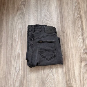 Svarta jeans från Lee, straight fit - Säljer ett par svarta jeans från Lee med klassisk femficksdesign och rak passform. De passar på nån som är mellan 169-175. Jeansen har en mörk tvätt med lätt slitning och Lee-logga på bakfickan samt läderpatch i midjan. Materialet är robust denim i bomull.