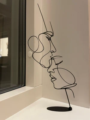 Tidlös och elegant ansiktsskulptur - Eterisk kyss-statyett  Denna minimalistiska skulptur i linjekonst ger ett sofistikerat och modernt uttryck till alla typer av rum. Det abstrakta ansiktet, format i en enda sammanhängande linje, skapar ett lugnt men samtidigt kraftfullt visuellt intryck. Perfekt för hem, kontor, hotell, receptioner och kreativa miljöer. En tidlös designpjäs som tillför personlighet och elegans utan att ta över rummet.  (Kan beställas i flera exemplar – 1, 3, 5 eller 10 stycken – till ett bättre pris.