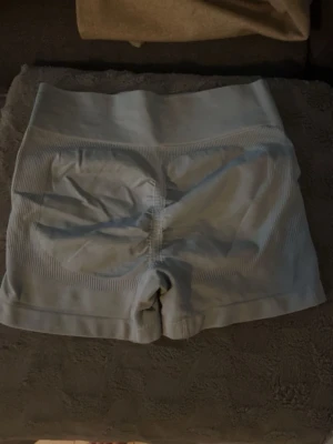 Ljusgrå seamless träningsshorts - Säljer ett par ljusgrå seamless shorts perfekta för träning. De är högmidjade med ribbade detaljer och har scrunch-effekt bak för extra form. Materialet är stretchigt och andas, vilket gör dem riktigt bekväma under intensiva pass.