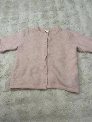 Ljusrosa stickad kofta med pärlknappar - Superfin ljusrosa stickad kofta i mjukt material. Rund hals, långärmad och stängs med pärlknappar framtill. Har använt ca 2 gånger som ny!