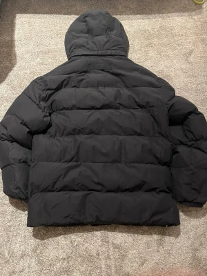 Svart gant jacka  - Säljer en riktigt fet gant puffer jacka. Jackan är i skick 8-10 och är använd i en vinter. Storlek 164 13/14 åringar. Hör av er vid mera frågor 