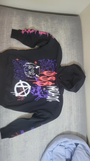 Svart hoodie FSBN XS med tryck - Svart oversized hoodie från FSBN i storlek XS med fet grafisk print i lila, rött och vitt på framsidan och ärmarna. Motiven inkluderar text, ansikte och skorpion. Mjuk bomullskänsla och stor huva för chill vibe.