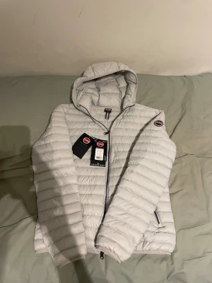 Vit dunjacka från Colmar med huva - Säljer en vit colmar jacka. Helt oanvänd men säljer den då den är för liten för mig och jag klippte av lappen så kan inte returnera jackan. Jag är 186 cm och den är lite för liten för mig. Den sitter som S/M, storlek 48. Jag har kvitto. Köpt för 2600. Skriv vid frågor kring jackan eller priset. 