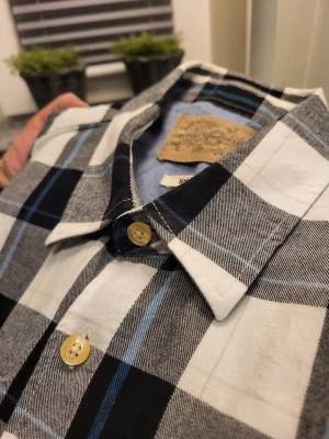 Vintage rutig skjorta från Valient Clothing M - Riktigt snygg rutig skjorta från Valient Clothing i svart, vitt, grått och blått. Skjortan har klassisk krage, bröstficka och gula knappar. Tillverkad i mjuk bomull och har långa ärmar. Perfekt för dig som gillar en chill och stilren look.