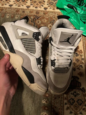 Nike Air Jordan 4 Retro vit/svart Äkta - Nike Air Jordan 4 Retro sneakers i vit och svart med grå detaljer. Skorna har klassisk meshpanel, snörning och Jumpman-logga på plösen och hälen. Ovandelen är i skinn och mocka, med platt sula och rund tå. Perfekt för dig som gillar ikoniska sneakers med streetkänsla. Kom med bud 