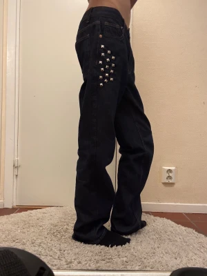 Mörkblå jeans med nitar - Säljer ett par mörkblå jeans med raka ben och coola silverfärgade nitar på vänster sida. Jeansen har klassisk femficksdesign, kontrastsömmar och normal passform. Materialet är robust denim som ger en snygg och tidlös look. Skriv för mer bilder. Innebredslängd 80cm, hör av er med frågor 🙏💕(jag står i en konstig position så det ser lite platt ut på första bilden)