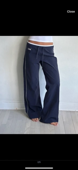Mörkblå wide byxor  - Snygga mörkblå wide byxor med vita kontrastlinjer längs benen och vit kant i midjan. Byxorna har låg midja och snörning framtill. Perfekta för en sportig och avslappnad stil.