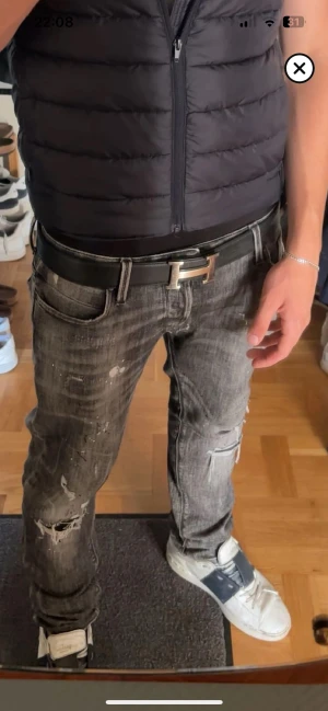 Jack & jones - Säljer ett par grå jeans med slitningar, hål och coola detaljer. Byxorna har en rak passform och klassisk femficksdesign. Färgen är mörkgrå med tvättade effekter och vita färgstänk. Perfekt för dig som gillar en edgy streetstil., dem är sönder vid gylfen men det går att sy igen