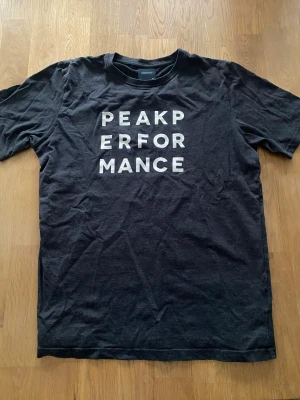 Svart Peak Performance t-shirt - Svart t-shirt från Peak Performance med vit text på bröstet. Klassisk rund hals och korta ärmar. Tillverkad i mjuk bomull som känns skön mot huden. Perfekt för dig som gillar enkel och stilren design.