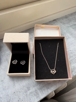 Smyckeset hjärta & evighet Guld Fynd - Säljer ett smyckeset från Guldfynd med matchande halsband och örhängen i silverfärgad metall. Båda har ett öppet hjärta med en evighetssymbol dekorerad med små glittrande stenar. Perfekt för dig som gillar stilrena och romantiska detaljer. Går att köpa separat 189kr st. Äkta silver! Nypris 580kr! 