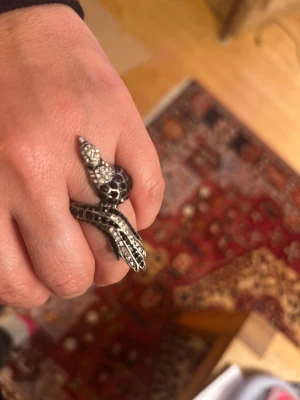 Svart påfågel med strassdetaljer - Cool ring i form av en påfågel gjord i svart metall med glittrande strass på huvudet och kroppen. Ringen har en unik design som verkligen sticker ut och passar dig som gillar edgy accessoarer. Perfekt för att ge din outfit en extra twist.