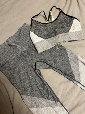 Matchande tränings sett - Snygga grå tights med olika grå nyanser och ribbade detaljer. De har hög midja och är tillverkade i ett mjukt, stretchigt syntetmaterial som sitter skönt mot kroppen. Perfekta för träning eller chill. Matchande sport-bh finns också.