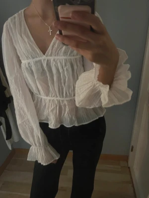 Vit blus med volangärmar från Gina Tricot - Säljer en superfin vit blus från Gina Tricot i storlek S. Blusen har v-ringning, volangiga långa ärmar och ett lätt transparent, krinklat tyg som ger en luftig känsla. Perfekt att styla med jeans eller kjol för en trendig look.