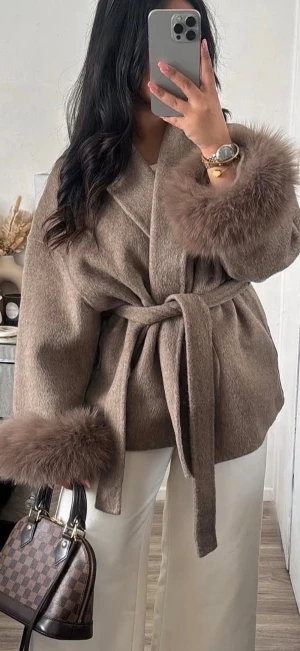 Beige kappa med pälsdetaljer och bälte - Säljer en beige kappa med breda pälsdetaljer vid ärmsluten och ett snyggt knytbälte i midjan. Jackan har en omlott-design och är tillverkad i mjukt ull och cashmere material. Köpte i London men den är tyvärr för kort i ärmarna och inte rätt storlek så därför säljer jag vidare. Nyskick! (Inte jag på bilderna) liten i storlek!