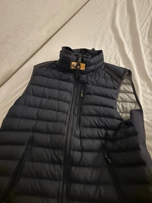 Svart dunväst från Parajumpers M - Säljer en svart dunväst från Parajumpers i storlek M. Västen är quiltad med hög krage, dragkedja framtill och snygg detalj med gul knapp vid halsen. Lättviktig och perfekt för lager-på-lager. Märke och äkthetslapp finns på insidan.säljer min väst på grund av att den ej passar. äkta.