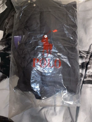 Svart pufferjacka från Polo Ralph Lauren - Säljer en svart pufferjacka från Polo Ralph Lauren med huva och dragkedja. Jackan har två fickor med dragkedja och den klassiska röda Polo-loggan på bröstet. Perfekt för kalla dagar och riktigt snygg till streetwear-stilen.