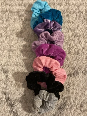 Färgglada scrunchies i sammet & glitter - Säljer ett set med åtta scrunchies i olika färger: ljusblå, mörkblå, lila, ljuslila, rosa, svart, silver och mörklila. Några är i mjuk sammet och andra i glittrigt material. Perfekta för att piffa till håret med en färgklick eller lite extra bling. Plus att dom går enkelt att tvätta i tvättmaskinen.