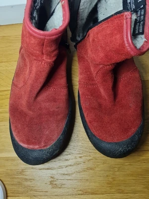 Röda mockaboots från Landrover stl 36 - Säljer ett par röda boots från Landrover i äkta mocka med svart sula och dragkedja på sidan. Insidan är fodrad med mjuk, vit polyester som håller fötterna varma. Perfekta för kyligare dagar och riktigt sköna att ha på sig.