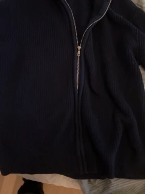 Mörkblå stickad kofta med dragkedja - Mysig mörkblå stickad kofta med hel dragkedja framtill. Perfekt för kyliga dagar och enkel att slänga på över en t-shirt. Klassisk ribbad struktur och tidlös design som funkar till det mesta.