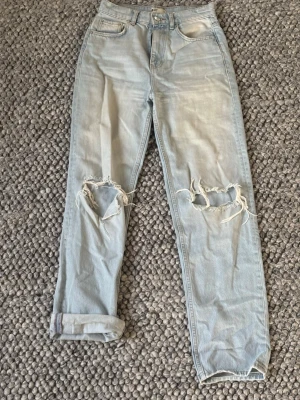 Ljusblå ripped straight jeans - Säljer ett par ljusblå jeans med raka ben och slitna hål över knäna för en riktigt avslappnad vibe. Hög midja och klassisk femficksmodell. Jeansen är i mjukt denimtyg. 
