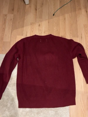 Vinröd stickad tröja Maison Margiela - Säljer en vinröd stickad tröja från Maison Margiela. Tröjan har en ribbad struktur, rund halsringning och långa ärmar. Perfekt för dig som vill ha en stilren och klassisk look med en twist av designer-vibe.