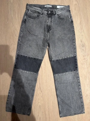  Our Legacy jeans - Säljer ett par grå jeans från Our Legacy med raka ben och coola mörkgrå patchar över knäna. Jeansen har klassisk femficksdesign, normal passform och är gjorda i denim. Perfekta för dig som gillar en unik och stilren look.