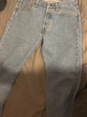 Levi's 501 ljusblå jeans W30 L30 - Klassiska Levi's 501 jeans i ljusblå tvätt med raka ben och normal passform. Jeansen har fem fickor, knappgylf och den ikoniska läderpatchen bak i midjan. Perfekta för en avslappnad och tidlös stil.