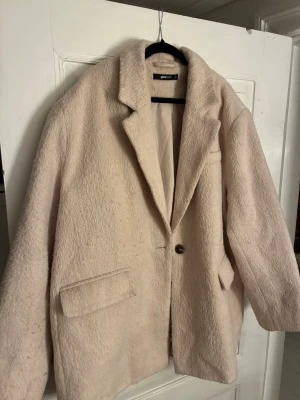 Beige teddyjacka från Gina Tricot XL - Säljer en oversized beige teddyjacka från Gina Tricot i storlek XL. Jackan har en mjuk och fluffig yta, klassisk krage, knäppning med en knapp och två stora fickor framtill. Perfekt för dig som gillar en chill och trendig look.