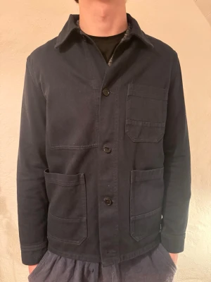  overshirt från Arket - Säljer en mörkblå overshirt från Arket med tre stora utanpåliggande fickor framtill och knäppning med svarta knappar. Jackan har klassisk krage och är tillverkad i ett kraftigare bomullstyg. Perfekt för lager på lager och enkel att styla. Nypris 1500 Mitt pris 299kr Storlek S Nyskick aldrig använd
