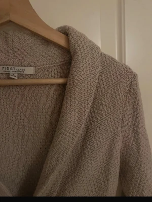 Beige stickad kofta från First Class - Mysig beige stickad kofta från First Class med avslappnad passform och långa ärmar. Storlek S - M