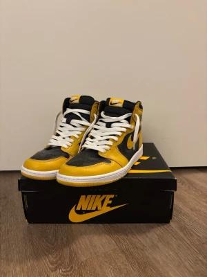 Nike Air Jordan 1 High Pollen - Nike Air Jordan 1 High sneakers i svart och gul med vit sula och vita skosnören. Klassisk high-top siluett med rund tå och platt sula. Ovandel i skinn med tydliga paneler. Använda ca 3 gånger