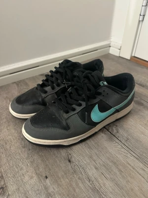 Nike Dunk sneakers svart/grå med turkos swoosh - Nike Dunk sneakers i svart och gråa och neon färg. Klassisk låg modell med svart snörning och vit mellansula. Perfekta för dig som gillar streetwear. Kvitto finns inte och priset är ej hugget i sten