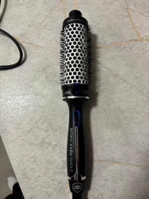 Björn Axén Tools varmluftsborste 38mm - Säljer en svart och silver varmluftsborste från Björn Axén Tools med keramisk och turmalinbeläggning. Borsten har rund form, integrerat joniseringssystem och blå detaljer vid knapparna. Perfekt för att styla håret med volym och glans.