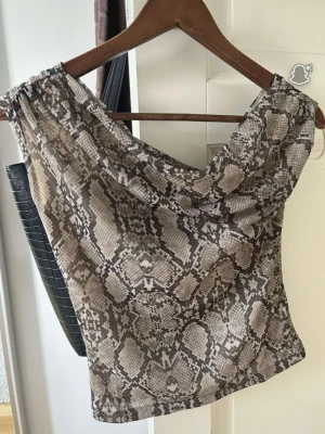 Ormmönstrad topp Gina Tricot  - Säljer en snygg off shoulder topp med ormmönster i beige och bruna toner. Helt oanvänd. 