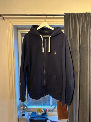 Ralph Lauren Polo zip Hoodie  - Polo Ralph Lauren herr huvtröja i storlek XL, färg blå, tillverkad i bomull. Tröjan har dragkedja fram, huva med dragsko och är designad för herrar. Finns inga skador eller hål, docklite urtvättade.  Hör av dig vid frågor! Kan diskutera pris vid snabb affär!